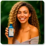 Smiling young woman with long, curly hair holding a bottle of Maui Moisture Coconut Milk Shampoo outdoors against a lush green background. She's wearing an off-the-shoulder striped top and looks joyful and confident