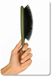 Close-up side view of a green flexible synthetic hairbrush held upright, highlighting curved design and soft, bendable bristles ideal for detangling curly hair.