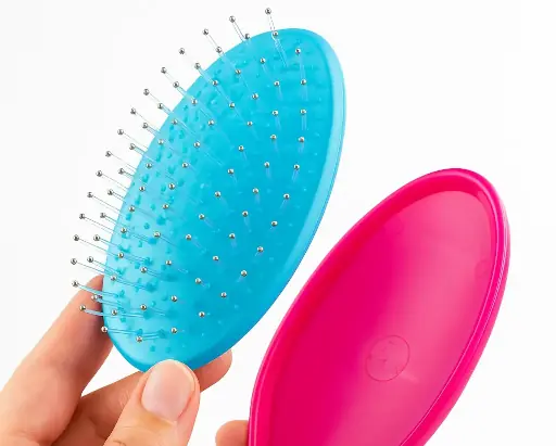 Close-up photo of a woman’s hands disassembling an Olivia Garden Detangler hairbrush for cleaning. One hand holds the turquoise bristle cushion, and the other holds the matte gray and pink brush shell. The image highlights the brush’s removable cushion feature for easy hygiene and maintenance, emphasizing cleanliness, durability, and thoughtful design in a well-lit studio setting